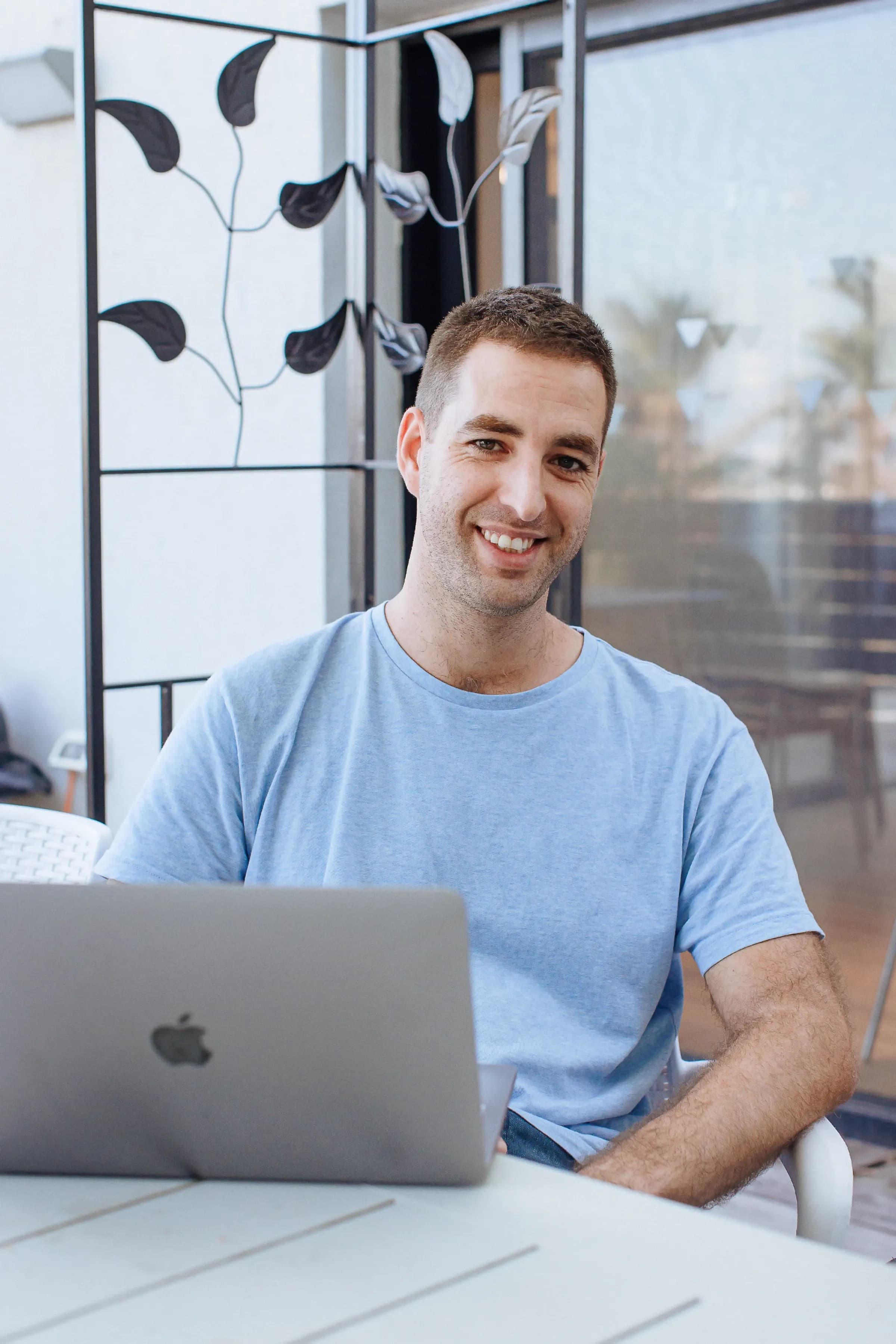 Smiling man seated at a table using a laptop.