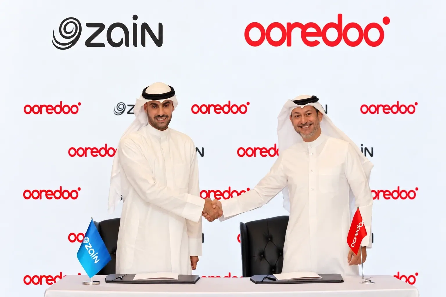 Two representatives shaking hands in front of Zain and Ooredoo branding.